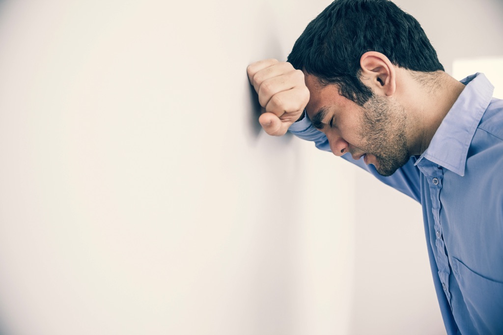Un hombre frustrado recarga su cabeza sobre la pared