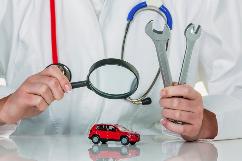 Persona con bata de doctor con dos herramientas de llave en una mano y en la otra está mirando con una lupa un carro pequeño