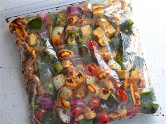 Corta los champiñones, el pimiento, la calabacita, los tomates enteros y la cebolla en cubitos de 1 pulgada y coloca todos los vegetales en una bolsa ziploc grande. Finalmente añade el balsámico y masajea la bolsa para incorporar las verduras con el balsámico 