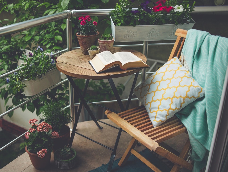 Balcón pequeño lleno de flores coloridas y un libro en una mesa pequeña