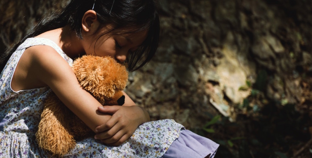 niña triste abrazando a un peluche