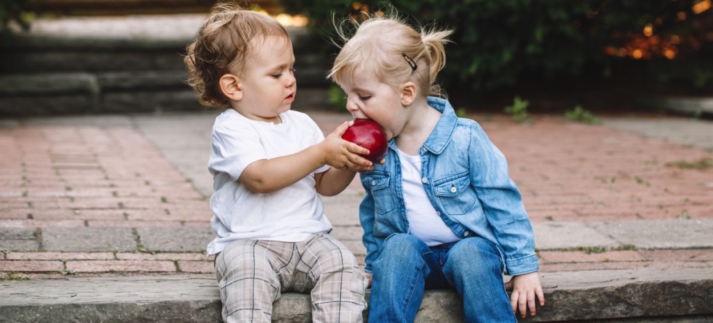 niño le da de comer una manzana roja a una niña