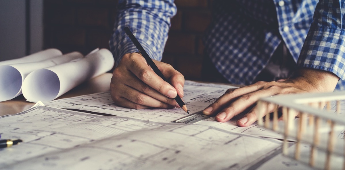 Un hombre dibujando con una regla en un plano de arquitectura