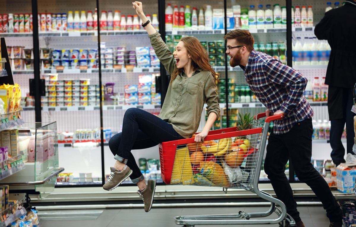 Pareja feliz jugando con el carrito en el supermercado 