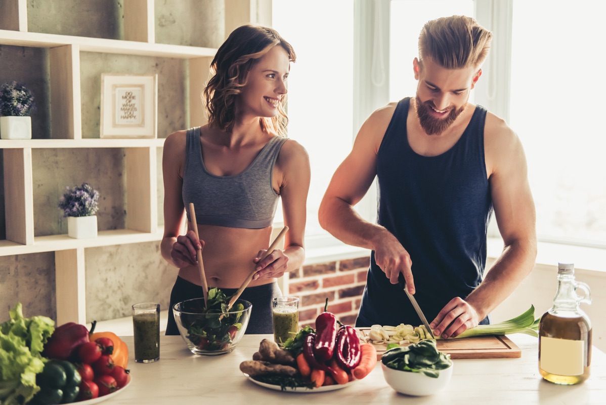Una pareja con ropa deportiva preparando una ensalada con frutas y verduras 