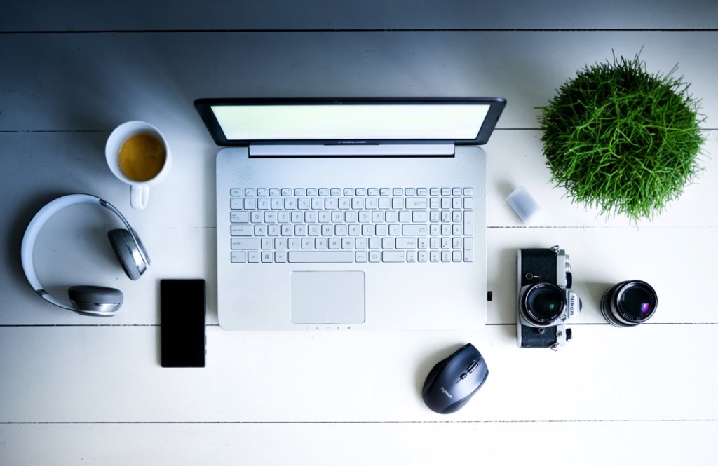 Escritorio con laptop, cámara, planta, lente, café, audífonos, mouse y celular 